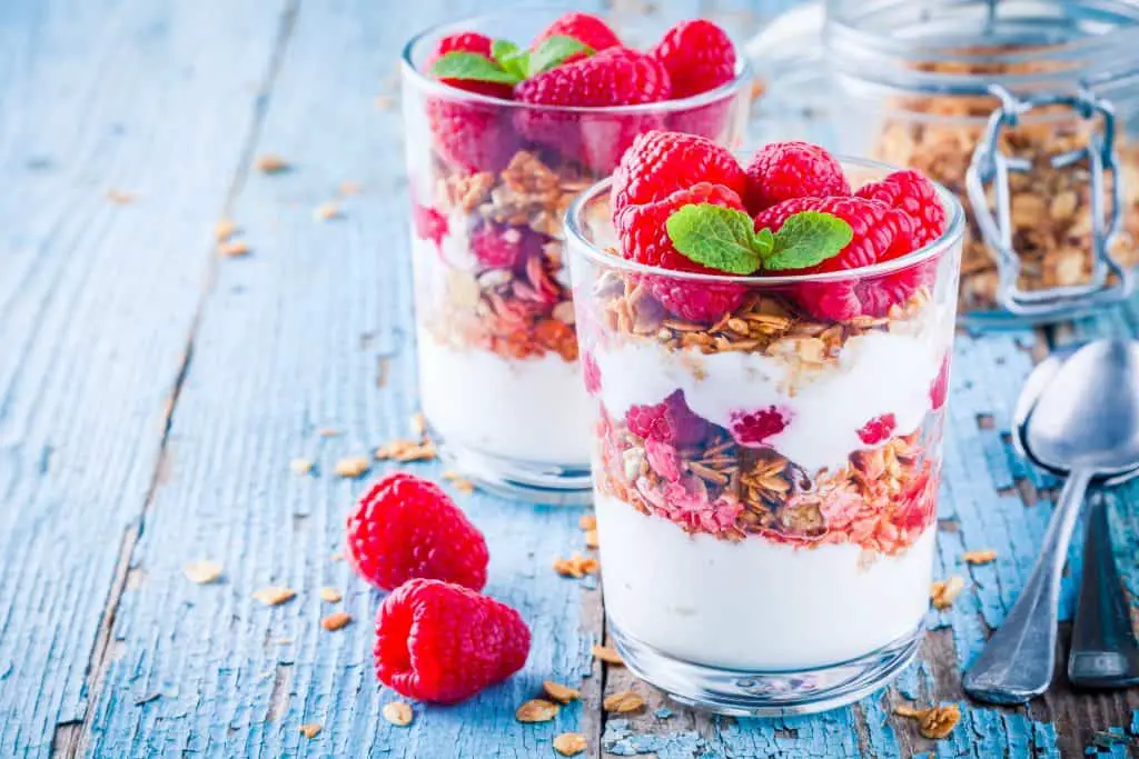 Healthy breakfast yogurt parfait with granola and fresh raspberries on rustic background