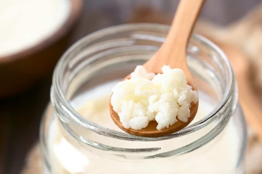 Milk kefir grains on wooden spoon on top of a jar of kefir