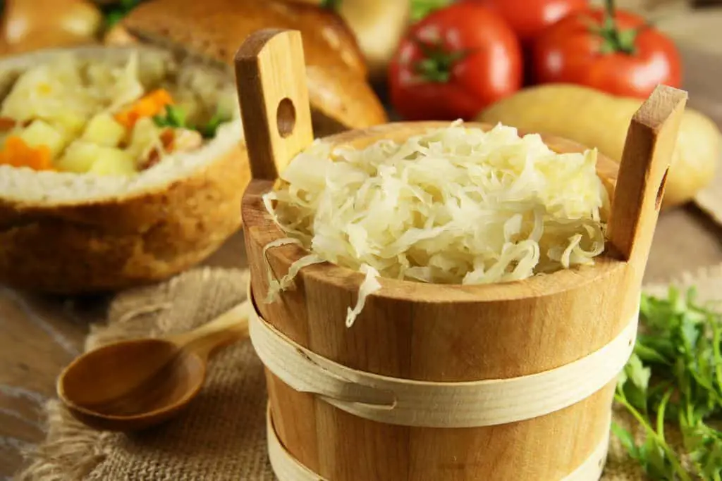 Sauerkraut in a wooden barrel and cabbage soup in the background