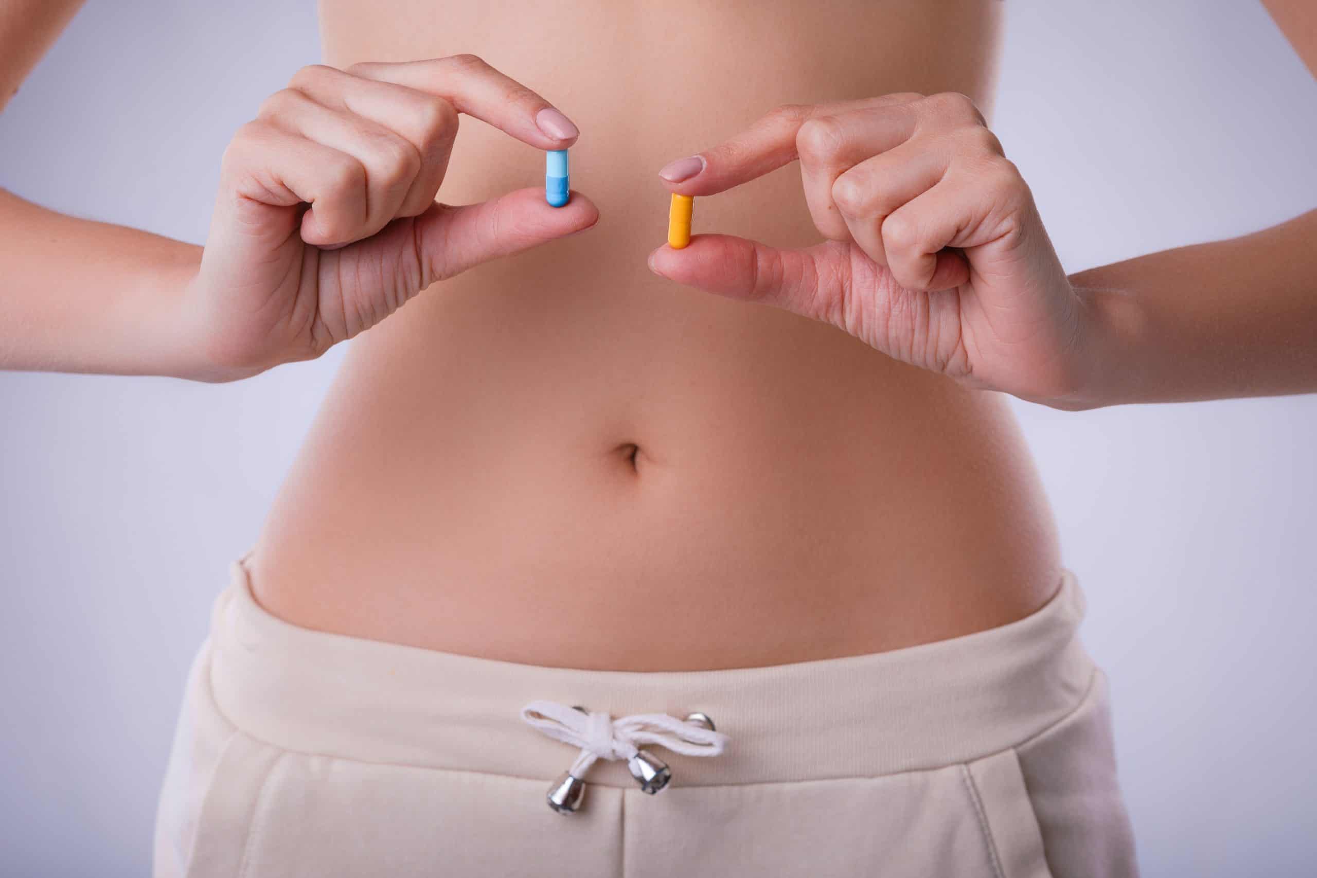 Pills with probiotics on the background of the female abdomen.