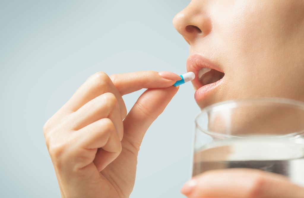 Woman taking a probiotic capsule with glass of water - probiotic before bed